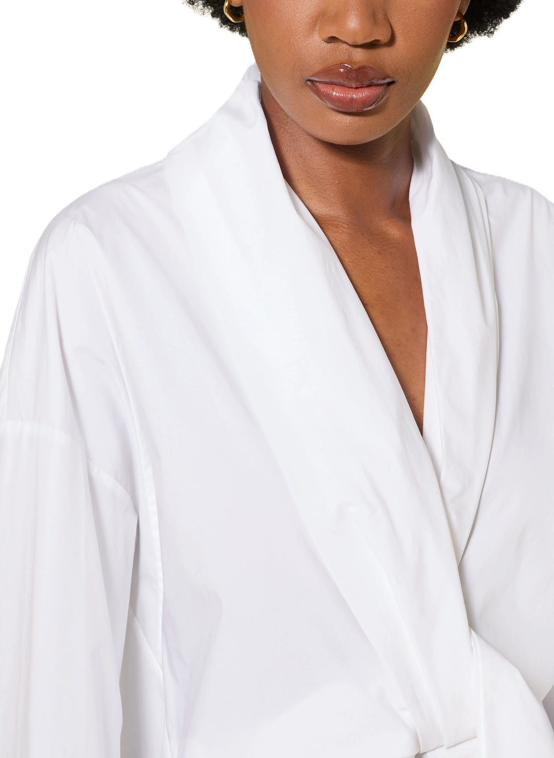 Bluse Dorothee Schumacher POPLIN POWER blouse in weiß. Diese Bluse ist ein richtiges It-Piece. Sie vereint modische Wickeloptik mit femininem Schnitt perfekt. Die Bluse hat einen Schalkragen und lange Ärmel. An den Manschetten befinden sich schöne Knöpfe. Die Ärmel sind weit und die Schultern überschnitten. Auf der Rückseite ist die Bluse eingeschlagen und der Saum mit einem elastischen Band versehen.