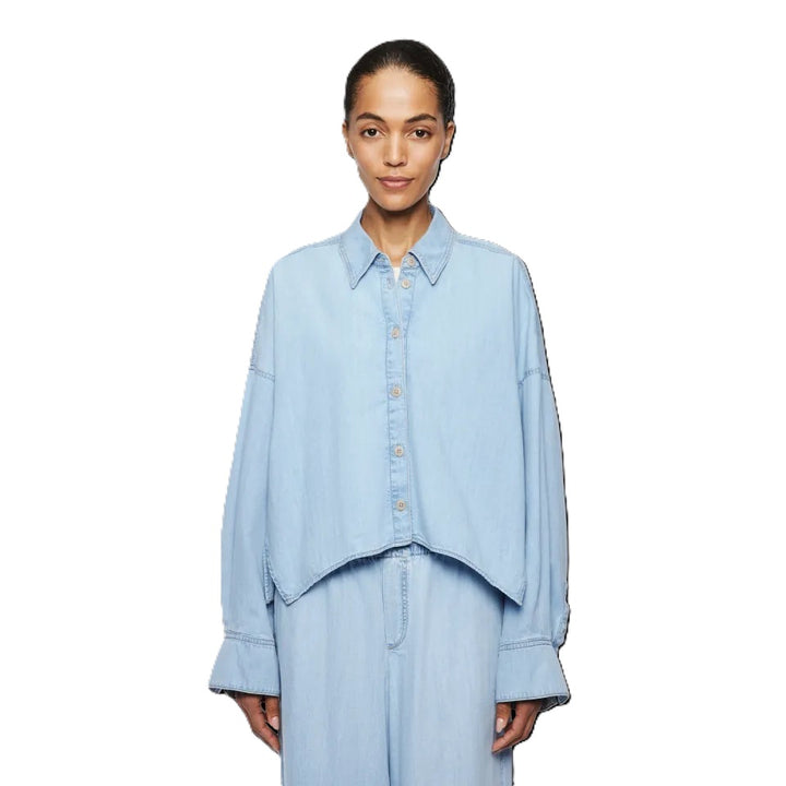 Bluse Drykorn OSHIA 10 in blau. OSHIA ist eine weit geschnittene Hemdbluse mit überschnittener Schulter und überlangen Ärmeln. Der Indigo Denim hat eine helle Farbgebung und einen leichten Wascheffekt was ihn zu einem echten Everyday Essential macht. Die Bluse hat einen Kragen und eine verdeckte Knopfleiste und ist vorne kürzer geschnitten als hinten.