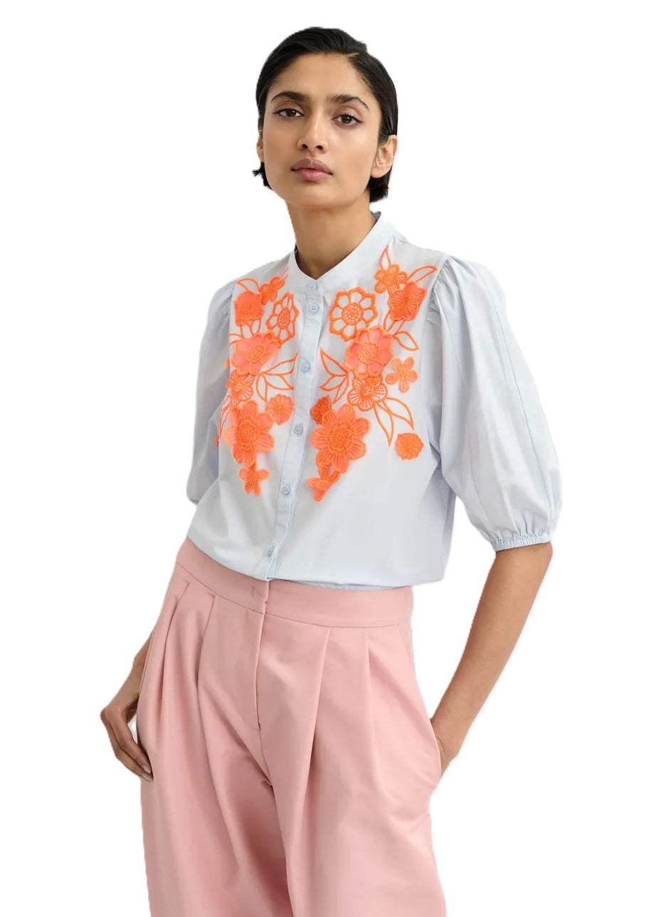 Bluse Essentiel Antwerp JORJA APPLIQUE FLOWER SHIRT. Bluse mit kurzarm und Blumenstickerei. Die Bluse hat einen Stehkragen und eine Knopfleiste. Der Saum hat einen Gummizug. Die Bluse ist blau, die Stickerei orange. 