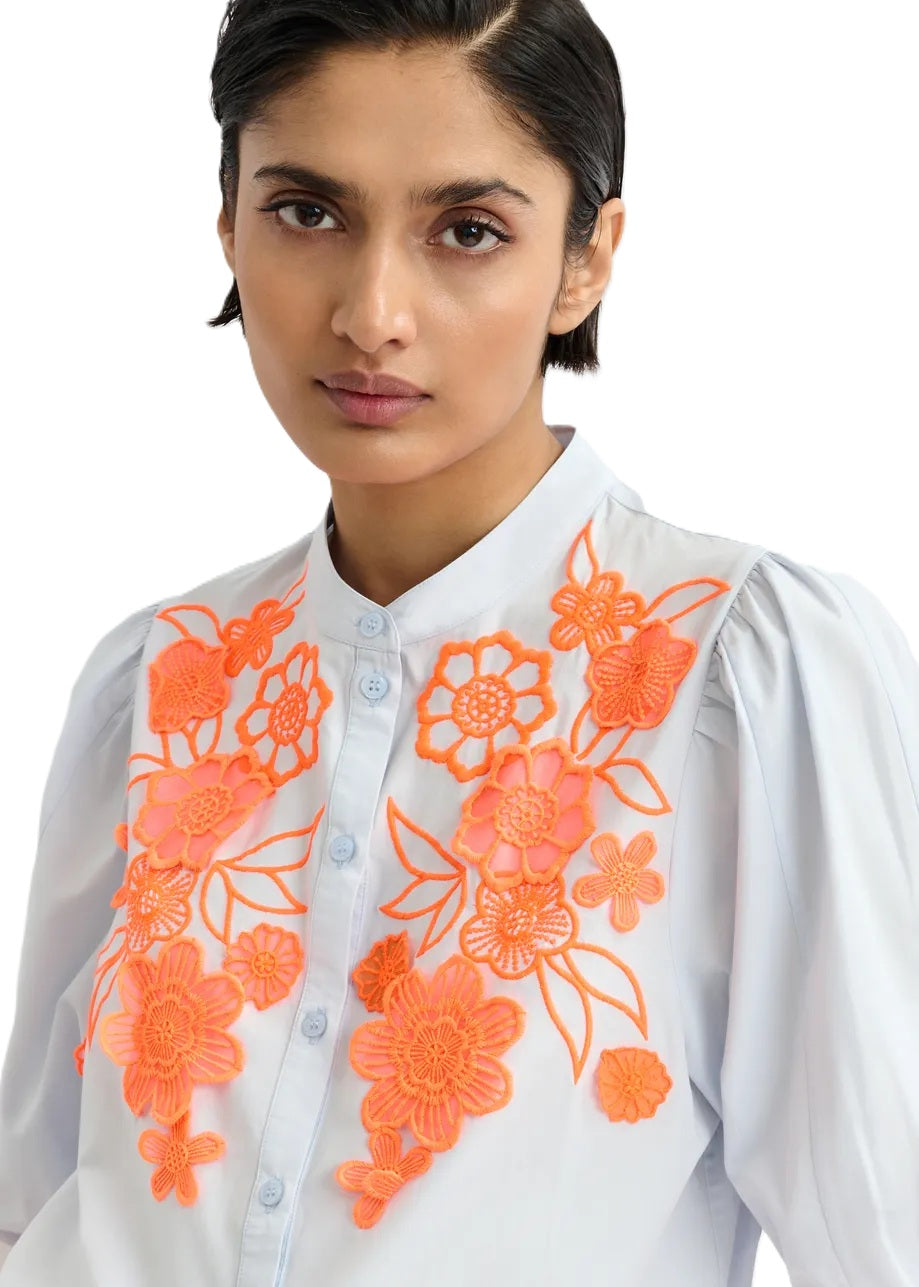 Bluse Essentiel Antwerp JORJA APPLIQUE FLOWER SHIRT. Bluse mit kurzarm und Blumenstickerei. Die Bluse hat einen Stehkragen und eine Knopfleiste. Der Saum hat einen Gummizug. Die Bluse ist blau, die Stickerei orange. 