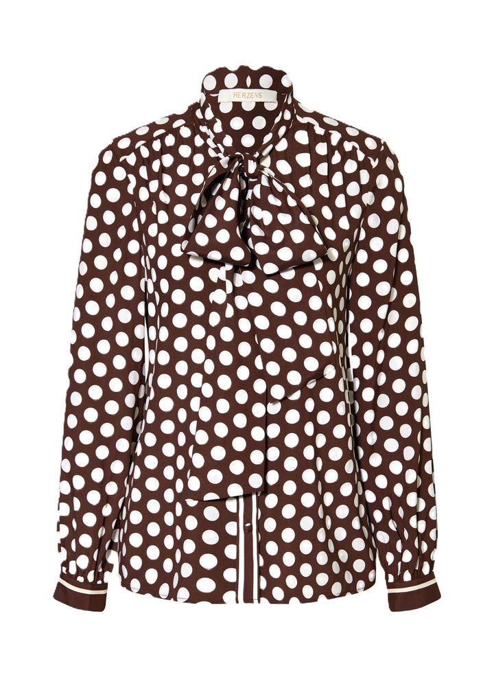Bluse Herzens. Schöne feminine Bluse mit Pünktchenmuster in braun weiß. Die Bluse hat eine Schluppe und schöne überzogene Knöpfe. Auch an den Manschetten sind die Knöpfe farblich passend überzogen. Die Ärmel sind lang und die Form gerade. An der Vorderseite sind leichte Falten eingearbeitet.