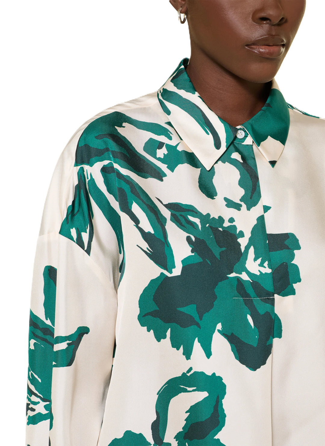 Bluse Herzens bottle green. Die hübsche Seidenbluse besticht durch ihr ausdrucksstarkes Muster. Der Unterton ist ecru und das Blumenmuster ist aus einem kräftigen Grünton. Die Bluse hat einen Kragen und eine halbe verdeckte Knopfleiste. Sie hat lange Ärmel mit breiten Manschetten und zwei Knöpfen. 