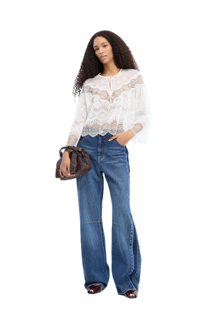Bluse Munthe VALIANCE in weiß. Wunderschöne transparente Spitzenbluse mit dekorativem Spitzenmuster. Die Bluse hat 3/4-Ärmel mit sanftem Volumen, einen runden Ausschnitt mit Knopfverschluss hinten sowie Bogenkanten für einen femininen und eleganten Look.