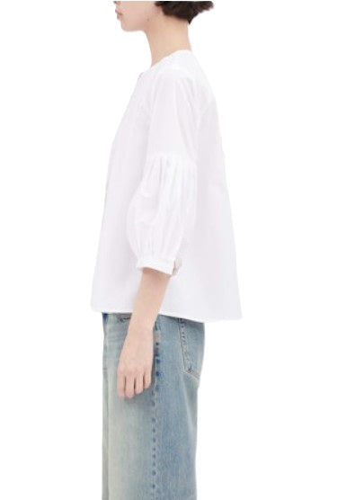Bluse von Odeeh in weiß mit 3/4 Ärmeln und Fältelung am Ärmel. Die Bluse ist ausgestellt, hat keinen Kragen und eine Knopfleiste aus Baumwolle. 
