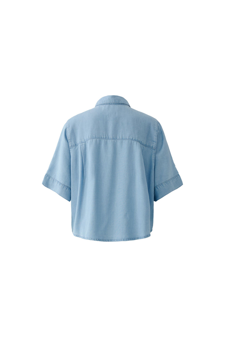 Bluse Oui. Schöne und sommerliche Halbarmbluse aus 100% Lyocell Denim. Die Bluse ist lässig geschnitten und hat eine reguläre Länge. Sie hat einen Kragen und eine Druckknopfleiste. Die Bluse hat einen weiten Kurzarm. Die Ärmel sind angeschnitten. Es befinden sich Kellerfalten links und rechts an der Rückenpasse. 