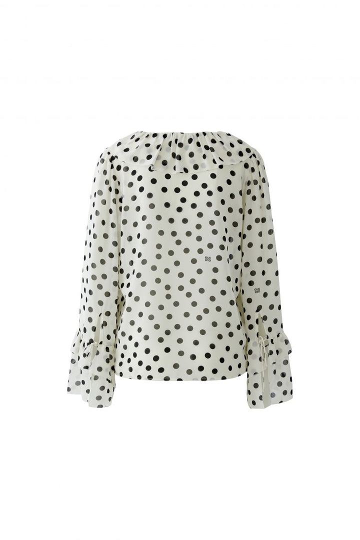 Romantische Rüschenbluse von Oui in ecru mit schwarzen Punkten. Die Bluse hat einen V-Ausschnitt mit Rüschen, ebenfalls Rüschen und Bändchen am Saum der Ärmel. 