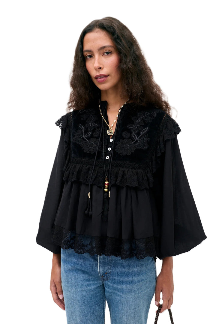 Bluse Rixo Diann Top in black. Ganz besondere Bluse in schwarz. Die Bluse hat einen verspielten romantischen Look mit Spitze und Samt. Die Bluse ist aufwendig mit Stickereien bestickt und hat kleine Spitzenflügel an den Schultern. Die Ärmel sind lang und haben eine Gummimanschette zum Hochshoppen. Sie hat einen V-Ausschnitt mit kleinen Knöpfen und Bändern mit Kordeldetails. 