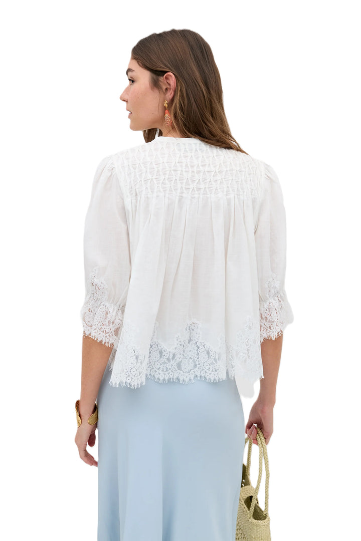 Rixo Erika Top ist eine Bluse in weiß mit Spitzenapplikationen a den Säumen. Sie hat eine Knopfleiste und einen Rundhalsausschnitt. 
