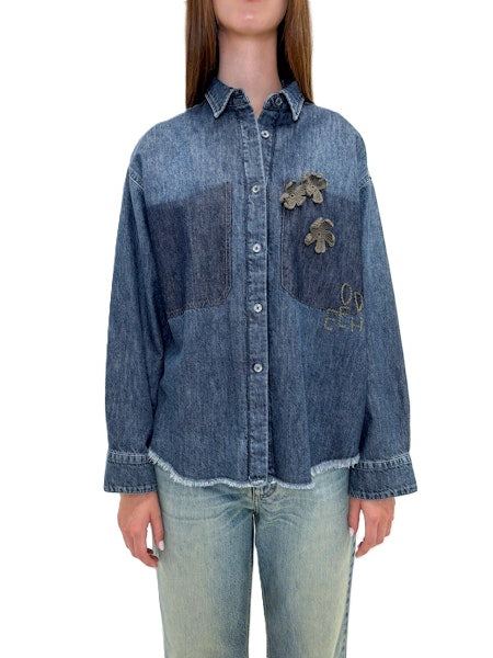 Jeansjacke von Odeeh in blau mit Blumenstickerei und Odeehlogo auf der Brust. Die Jacke hat einen Kragen,, Knöpfe und ausgefranste Säume. Sie fällt normal aus. 