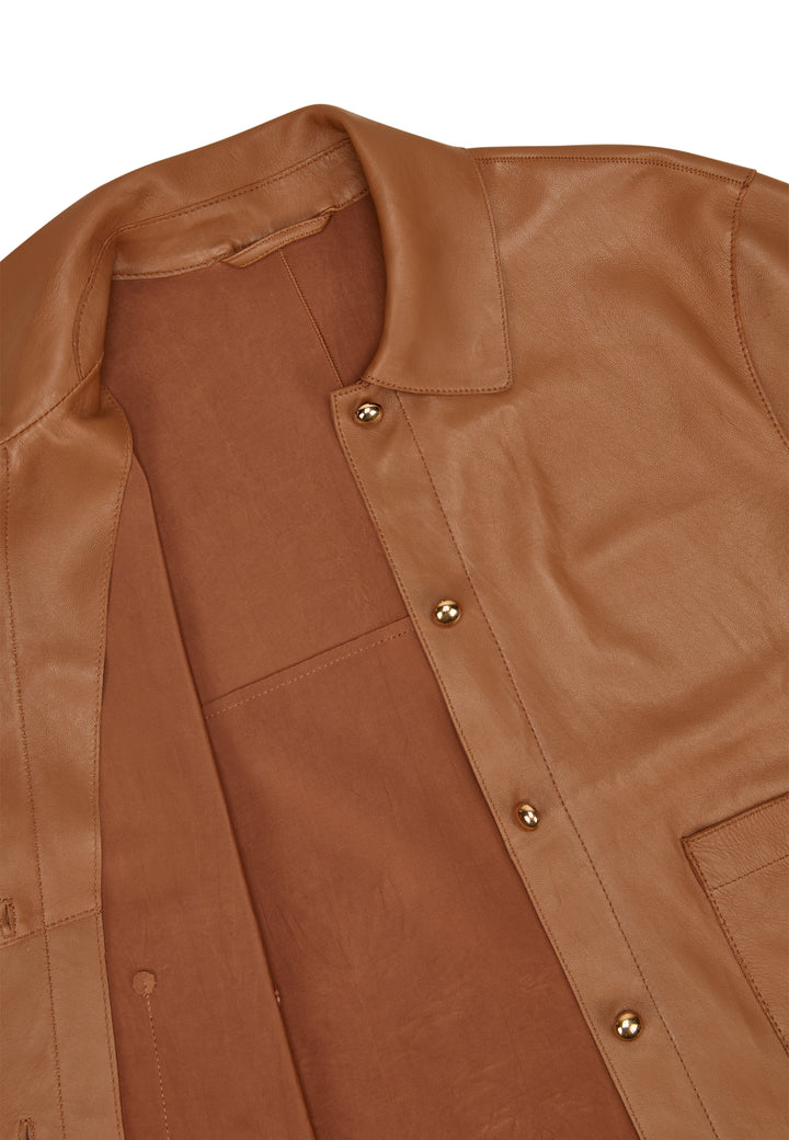 Jacke Milestone MSBetty in cognac. Wunderschöne Jacke aus feinem Lamm Nappa. Die Jacke ist bondiert mit tonigem Lycra Jersey. Sie ist geschnitten wie ein kurzes Hemd mit Knöpfen. Die Form ist gerade. Die Jacke hat einen Hemdkragen und einen Knopfverschluss. Ebenso zwei aufgesetzte Taschen mit Knopf. Die Ärmel sind kurz und die Schultern leicht überschnitten. An der Seitennaht befindet sich ein kleiner Schlitz. 