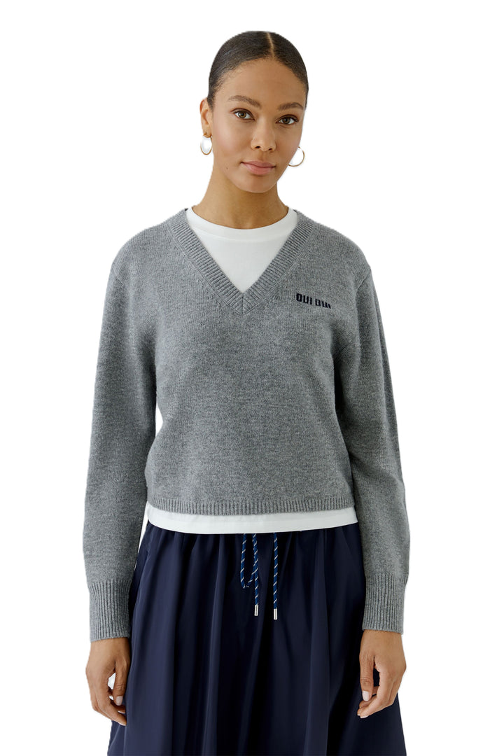 Grauer Pullover von Oui im Preppy Look mit V-Ausschnitt und Jersey-Details. Der glatt gestrickte Pullover hat noch ein kontrastfarbenes Oui-Logo.